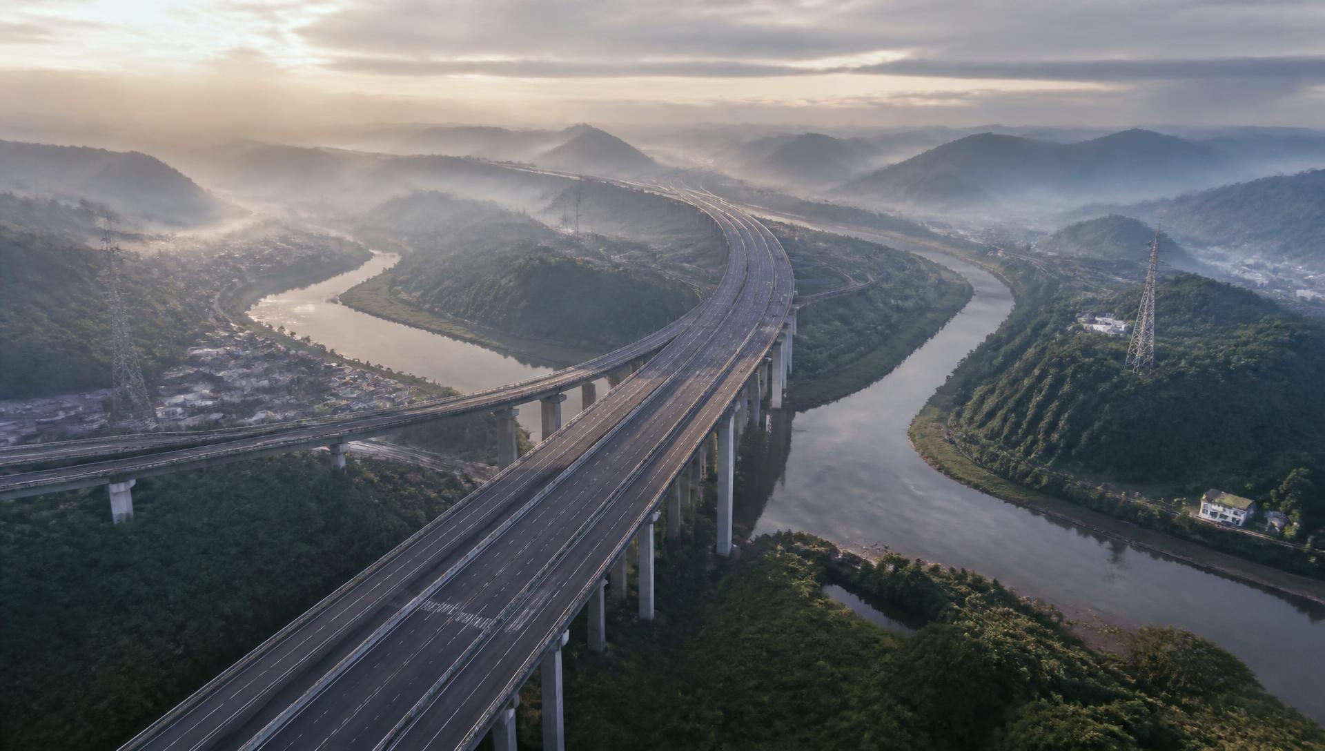 Aerial view of a completed expressway corridor crossing a river valley at dawn